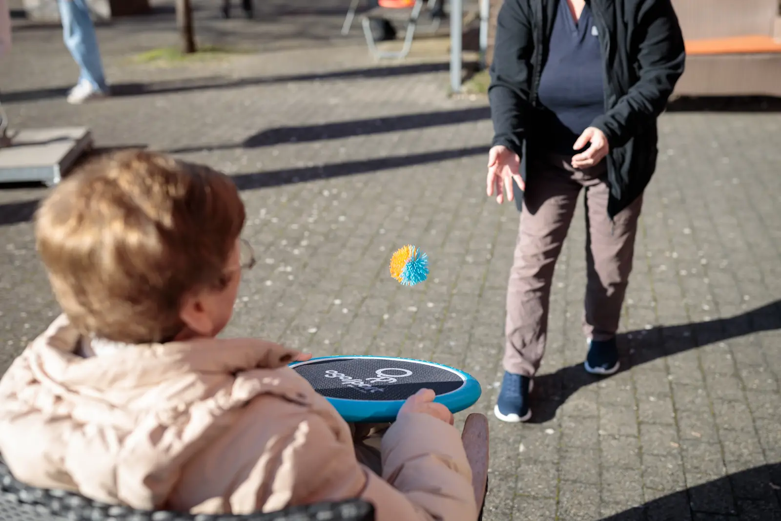 Zwei Besucherinnen des Tagesheimes spielen ein Ballspiel draussen im sonnigen Garten.