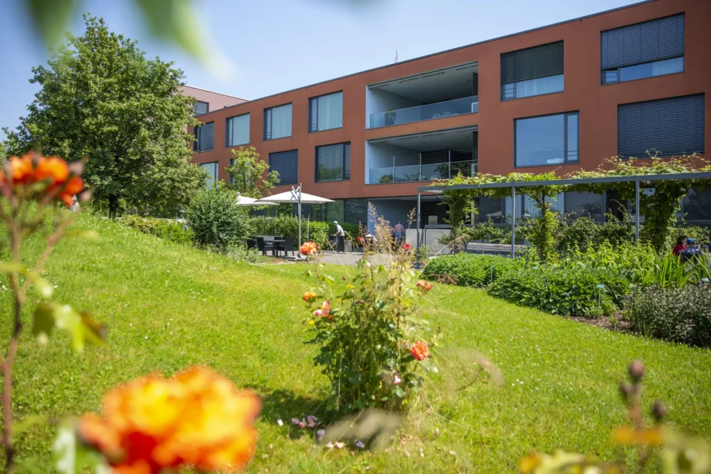 Bluehender Garten mit schattigen Sitzplaetzen und gepflegten Gruenflaechen vor dem Pflegezentrum Baar.