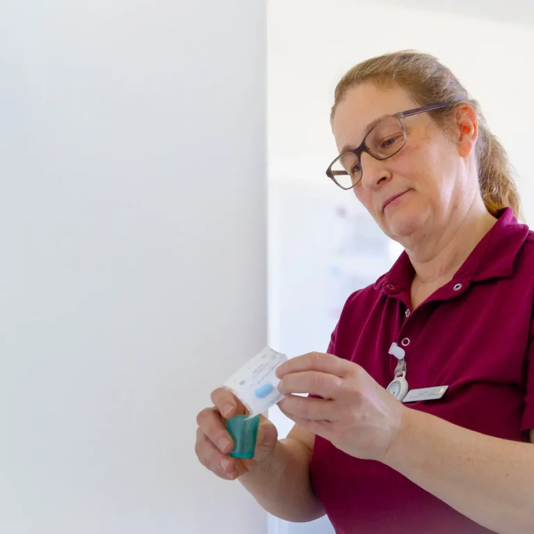 Portrait einer lächelnden Mitarbeiterin des Pflegezentrums Baar in Dienstkleidung, die ein Medikament betrachtet.