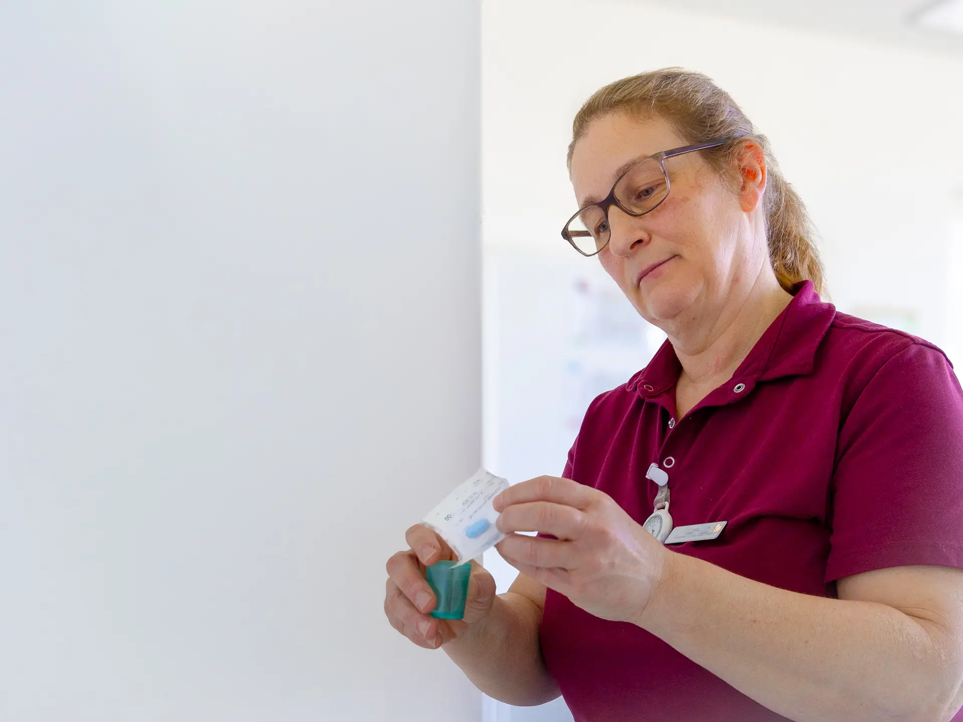 Portrait einer lächelnden Mitarbeiterin des Pflegezentrums Baar in Dienstkleidung, die ein Medikament betrachtet.